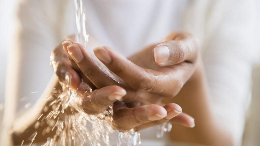 Ein Mädchen, das seine Handflächen unter einem Wasserstrahl wäscht.