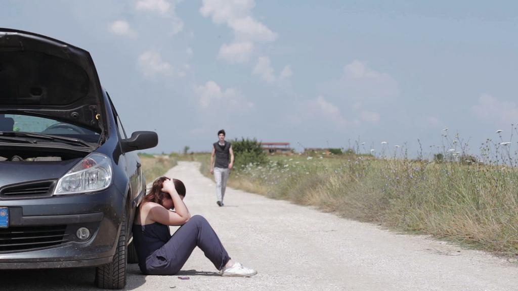 Mädchen sitzt neben einem kaputten Auto