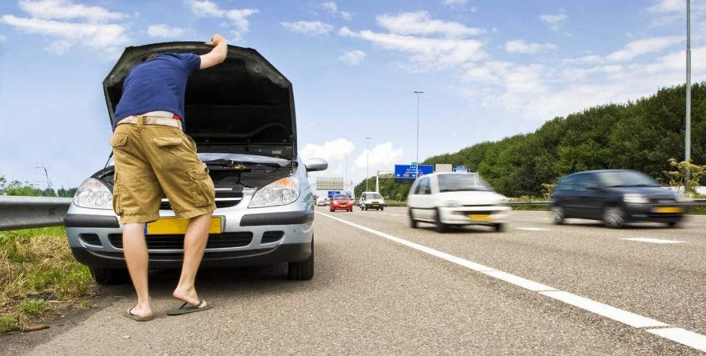 ein Mann schaut unter die Motorhaube eines liegengebliebenen Autos